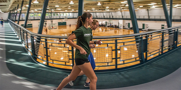 Two young women running on indoor track.