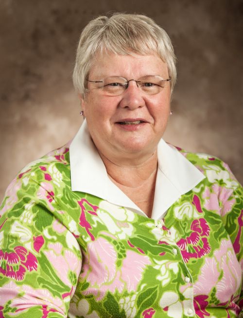 Photo of Sandra Geller smiling at camera on portrait background has white hair and glasses with stud earrings on