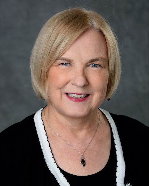 Image of Terrie Wehrwein smiling at camera on portrait backdrop has short blonde hair